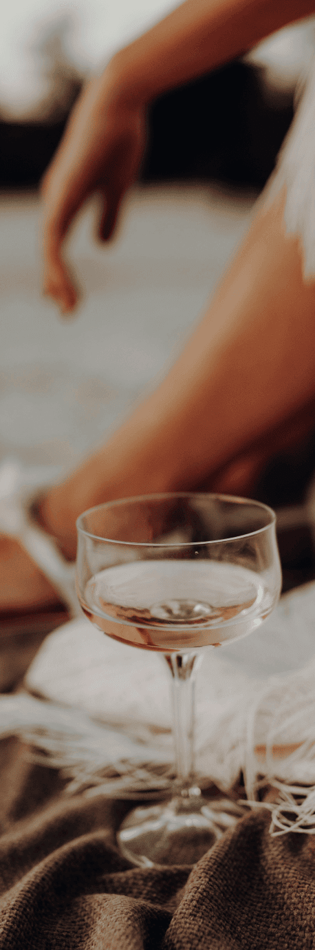 A person sits on a blanket, savoring a glass of rosé wine in the foreground, embodying effortless elegance and timeless branding.