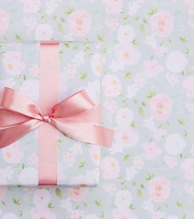 Gift wrapped in floral paper with a pink ribbon, placed on matching floral background.