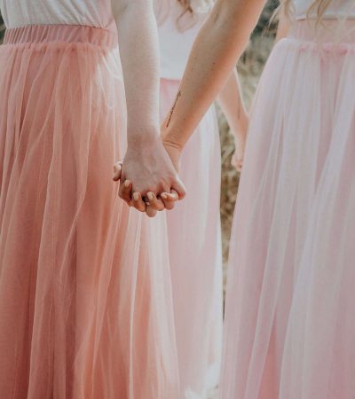 Two people in light pink skirts holding hands, symbolizing a harmonious collaboration, outdoors.