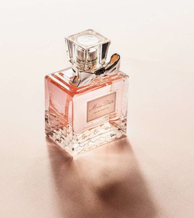 A clear glass bottle of pink perfume with a silver cap sits elegantly on a light surface, perfect for those considering rebranding their fragrance collection.