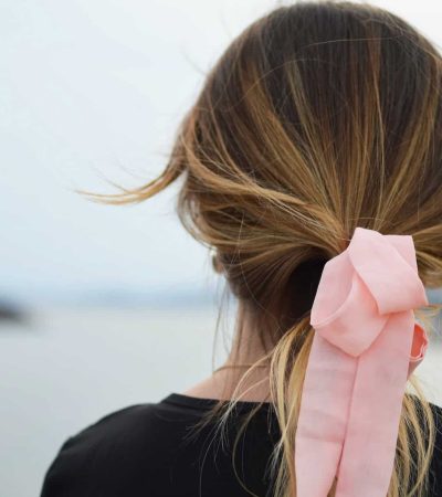 A person with long hair tied in a pink bow faces a body of water, reflecting on overcoming self-doubt.